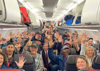 Group of veterans and guardians waving from inside the airplane during an Honor Flight trip.