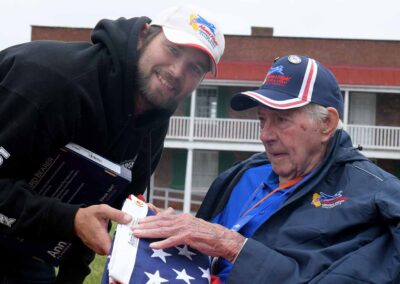 "A veteran and their guardian hold the flag that was raised at Fort McHenry, standing in front of a historical backdrop and reflecting on its deep connection to the history of American freedom and resilience."